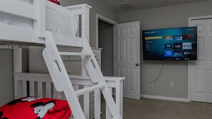A child's bunk bed with a Mickey Mouse pillow, a television mounted on the wall displaying a Roku TV interface, and a closed door in the background. - 5BR Veranda Palms Home Near Disney for 14 (Kissimmee)