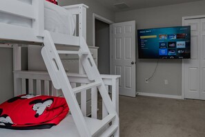 Ein Kinderstockbett mit einem Mickey Mouse Kopfkissen, ein an der Wand befestigter Fernseher mit Roku TV Anzeige und eine geschlossene Tür im Hintergrund.