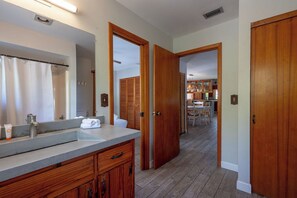 A bathroom with a large mirror, a sink, and wooden cabinets. There is a hallway leading to a dining area with a table and chairs. - Tree Top Bungalow: 2-min walk to beach access, Private Pool (Anna Maria)
