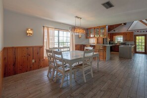 A spacious dining area with a large wooden table and chairs, a kitchen with wooden cabinets, and a view of the outdoors through the windows. - Tree Top Bungalow: 2-min walk to beach access, Private Pool (Anna Maria)