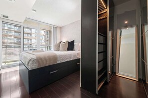 Un dormitorio moderno con una cama grande, almacenamiento integrado y vistas de la ciudad a través de ventanas de piso a techo.