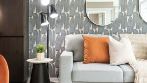 Ein modernes Wohnzimmer mit einem grauen Sofa, einem runden Spiegel und einer Stehlampe mit drei Leuchten.