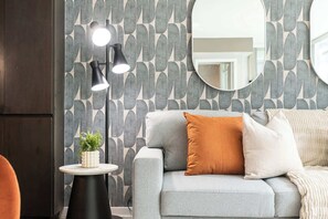 Un salón moderno con un sofá gris, un espejo redondo y una lámpara de pie con tres luces.