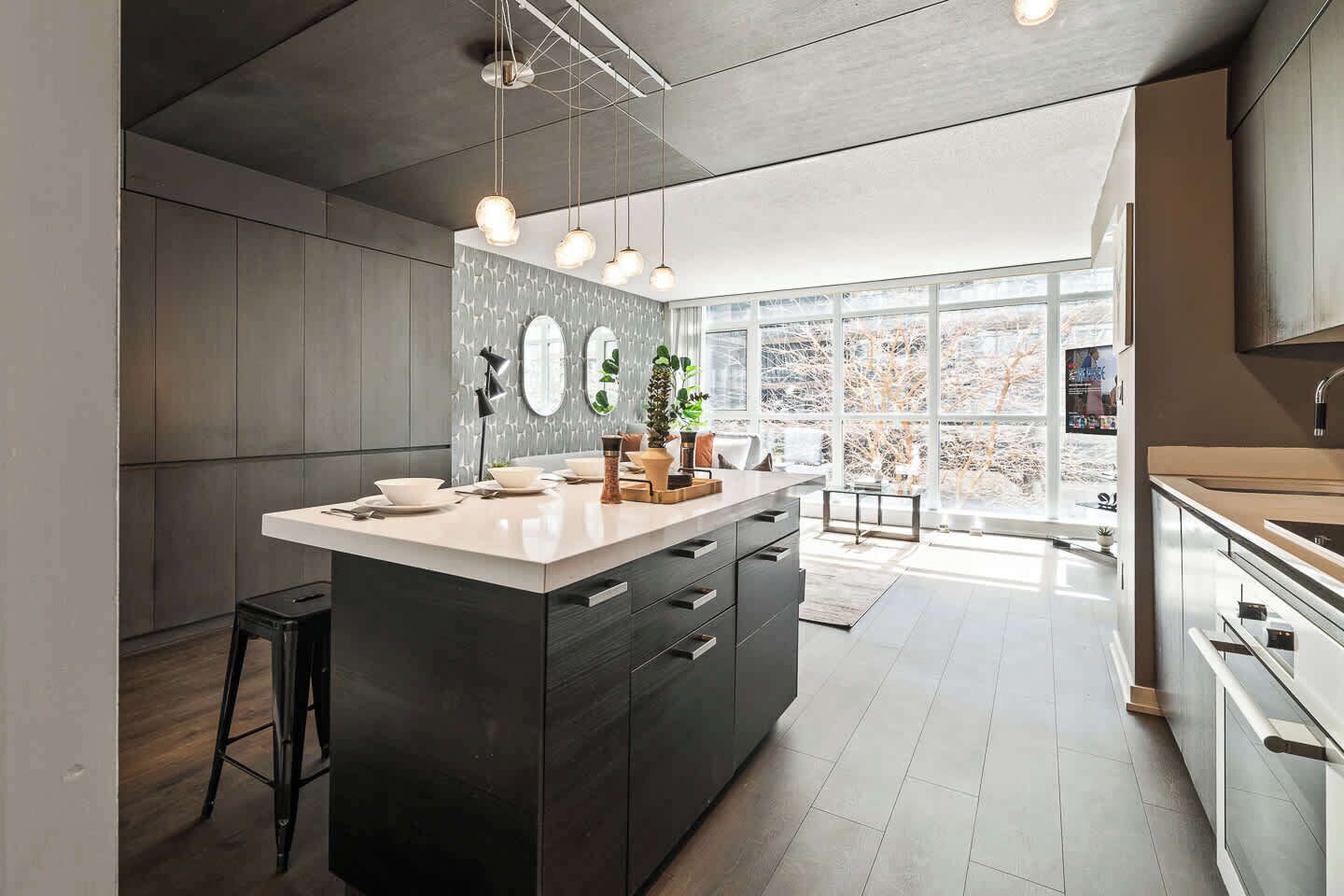 A modern kitchen with a large island, dark cabinetry, and a view of a snowy landscape through large windows.