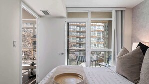 Ein Schlafzimmer mit großem Fenster, einem Bett, einem Nachttisch und einem Sessel.