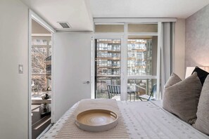 Un dormitorio con un ventanal grande, una cama, una mesita de noche y una silla.