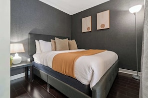 A modern bedroom with a bed, nightstand, lamp, and two wall-mounted picture frames. - Stunning Condo Near CN Tower & Waterfront Parking | Parking Available (Toronto)