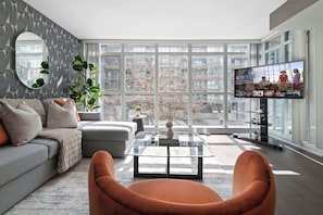 A modern living room with a large window, a sofa, a coffee table, and a television. - Stunning Condo Near CN Tower & Waterfront Parking | Parking Available (Toronto)