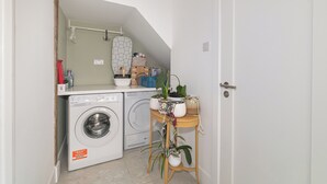 Een kleine wasruimte met een wasmachine, een droogrek en een tafeltje met planten.
