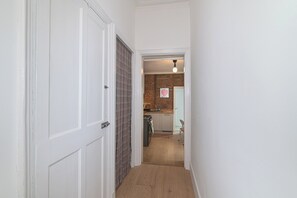 Ein schmaler Flur, der zu einer Küche führt, mit einer Ziegelwand, einer Hängeleuchte und einer Tür mit einem Karomuster-Vorhang.