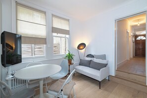 A modern living room with a white sofa, a round dining table, and a TV. - Stylish, cozy Refurbished Flat Near Stratford - Pass the Keys (London)