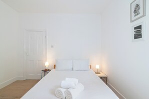 A hotel room with a bed, two bedside lamps, a door, and two framed pictures on the wall. - Stylish, cozy Refurbished Flat Near Stratford - Pass the Keys (London)