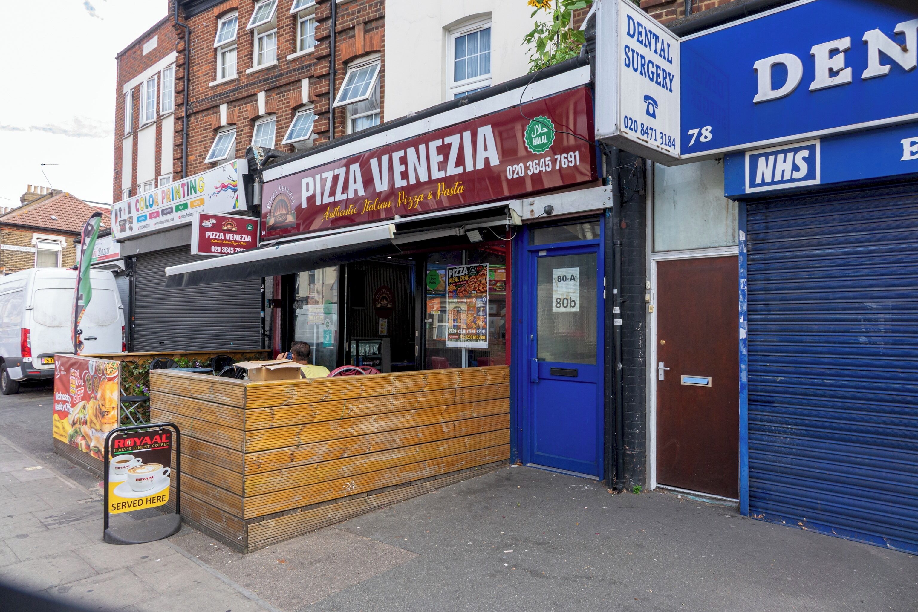 Un restaurant de pizzas avec une enseigne, une porte bleue et un volet bleu fermé sur le côté droit.