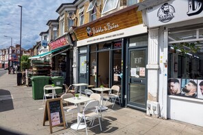 A street with outdoor seating, a food and wine shop, and a hair salon. - Stylish, cozy Refurbished Flat Near Stratford - Pass the Keys (London)