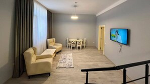 Una sala de estar con sofá, una mesa de centro, televisor montado en la pared y un comedor con sillas y mesa.