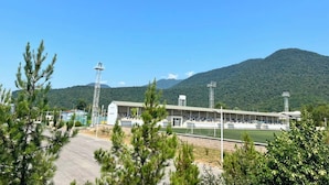 Un estadio con pista de atletismo, rodeado de árboles y una montaña al fondo.