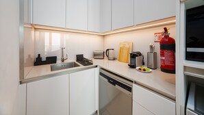 A modern kitchen with white cabinetry, a stainless steel sink, a Bosch dishwasher, a toaster, a kettle, a coffee maker, a fire extinguisher, and a knife block. - Chic Address JBR Haven w/ Marina View (Dubai)