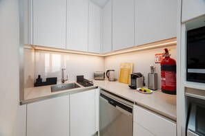 Eine moderne Küche mit weißen Schränken, einer Edelstahl-Spüle, einem Geschirrspüler von Bosch, einem Toaster, einem Wasserkocher, einer Kaffeemaschine, einem Feuerlöscher und einem Messerblock.