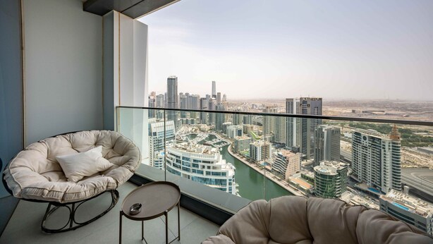 A balcony with a city view, a cushioned chair, and a small table. - Chic Address JBR Haven w/ Marina View (Dubai)