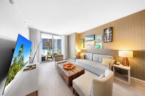 A modern hotel room with a large window, a sofa, a coffee table, a TV, and artwork on the wall.
