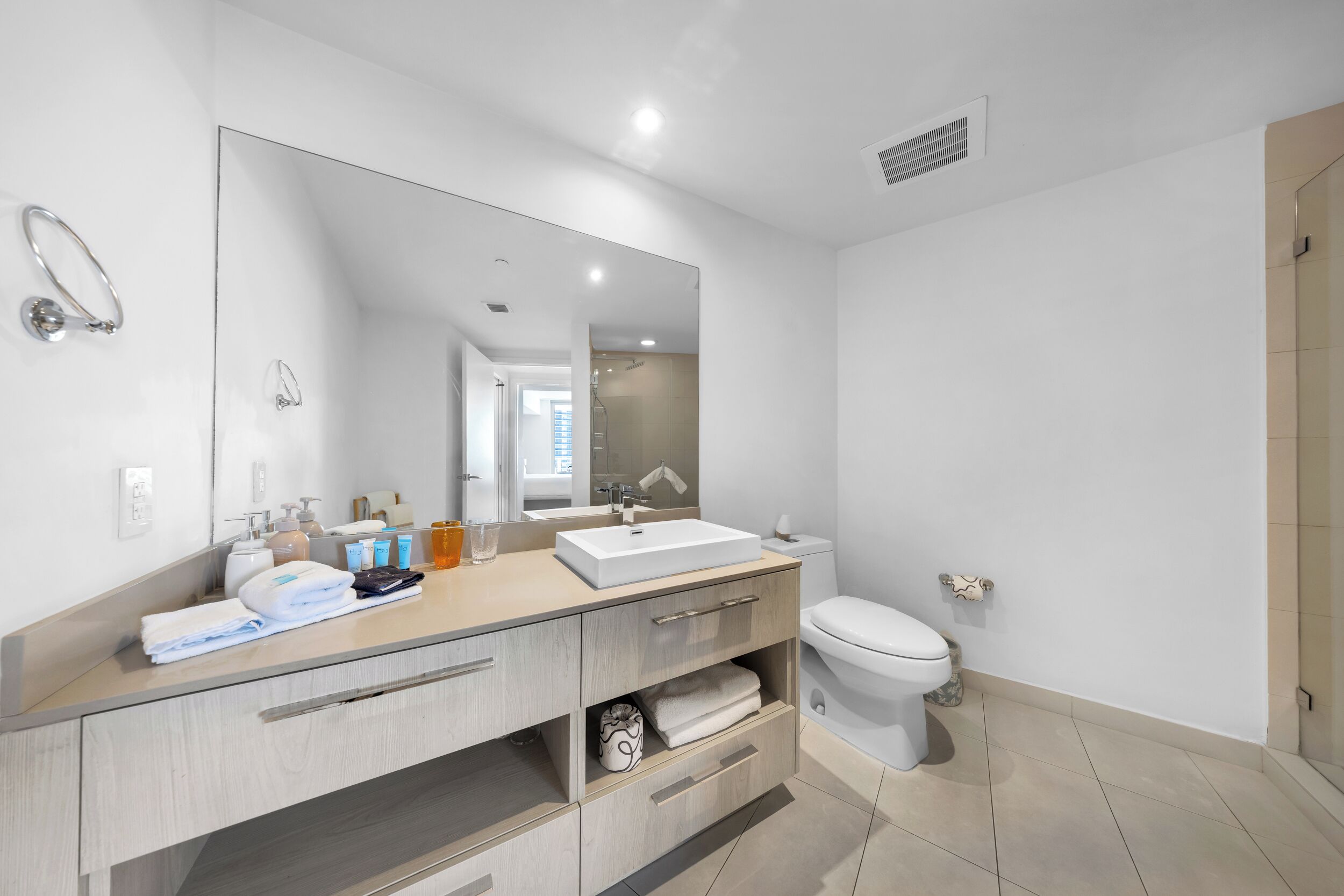 A modern bathroom with a large mirror, a white sink, a toilet, and a shower area.
