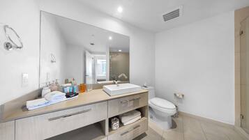 A modern bathroom with a large mirror, a white sink, a toilet, and a shower area.