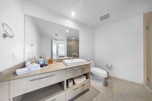 A modern bathroom with a large mirror, a white sink, a toilet, and a shower area.