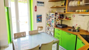 Uma cozinha com bancada verde, mesa de vidro e geladeira coberta de adesivos.