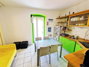 A compact kitchen with a dining area, green cabinets, and a refrigerator covered in magnets.