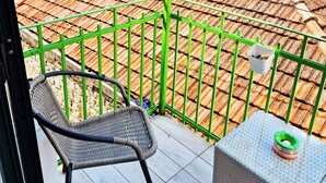 Varanda com cadeira de vime e uma mesa pequena, com vista para telhados de azulejos e edifícios de pedra.