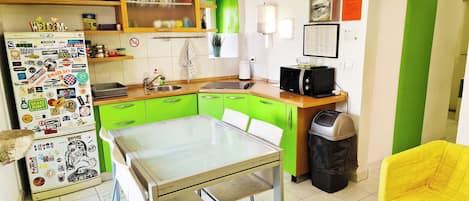 A compact kitchen with a dining table, green cabinets, a microwave, and a trash bin.