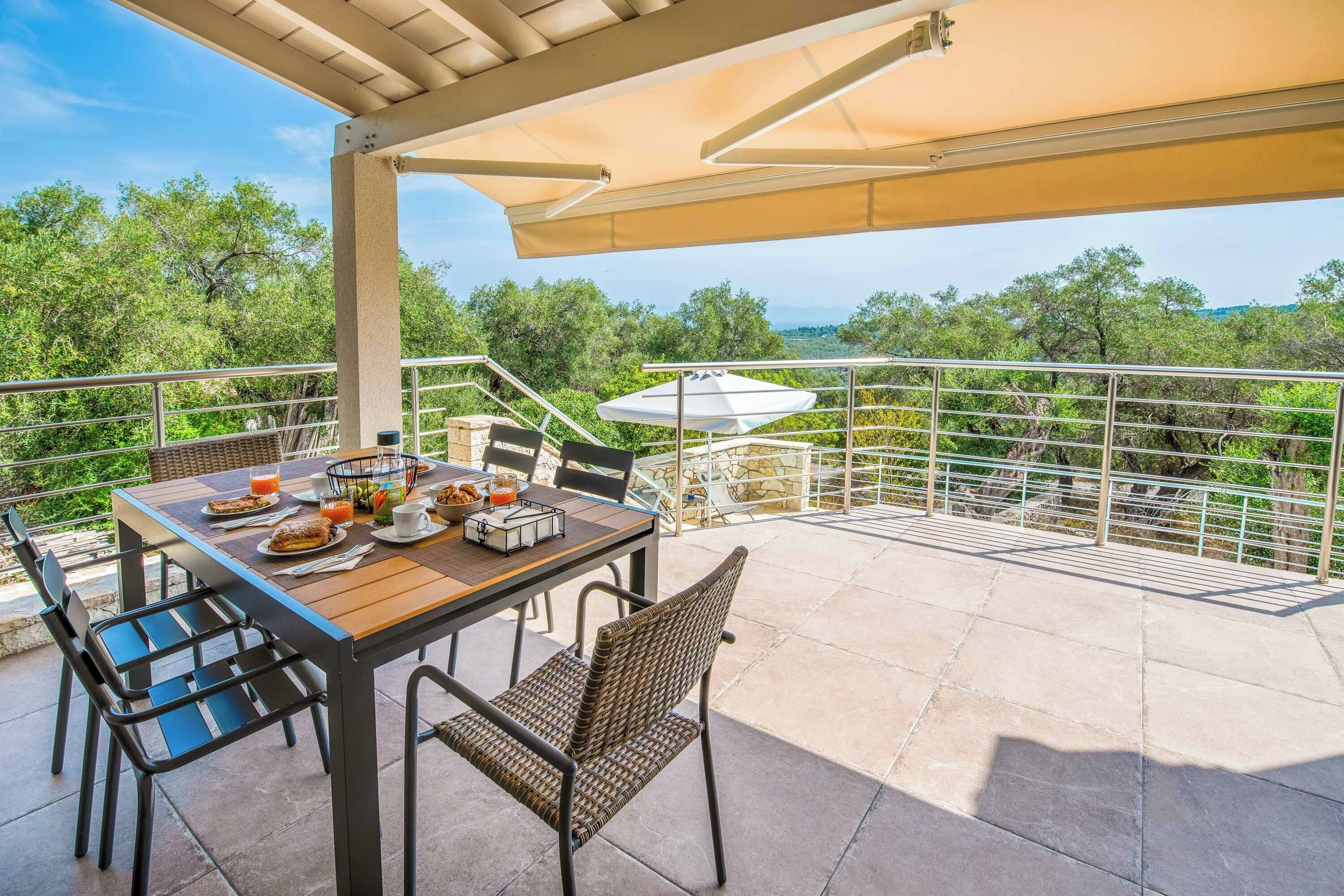 Une terrasse extérieure avec une table dressée pour le petit-déjeuner, entourée de chaises et d’une rambarde.