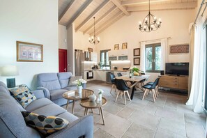 A modern living room with a sofa, coffee table, and dining area. - Villa Ares - Three Bedroom Villa, Sleeps 6 (Paxi)