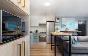 A modern kitchen with a built-in oven, a refrigerator, and a dining area with a table and chairs. - Cape on Viola | Modern Apartment in Table View (Cape Town)