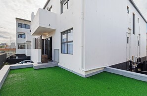 A modern building with a flat roof, a small front yard with artificial grass, and a visible door. - Cape on Viola | Modern Apartment in Table View (Cape Town)