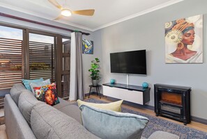 A modern living room with a sofa, television, artwork, and a fireplace. - Cape on Viola | Modern Apartment in Table View (Cape Town)