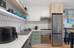 A modern kitchen with a built-in dishwasher, a stainless steel refrigerator, and a gas stove. - Cape on Viola | Modern Apartment in Table View (Cape Town)