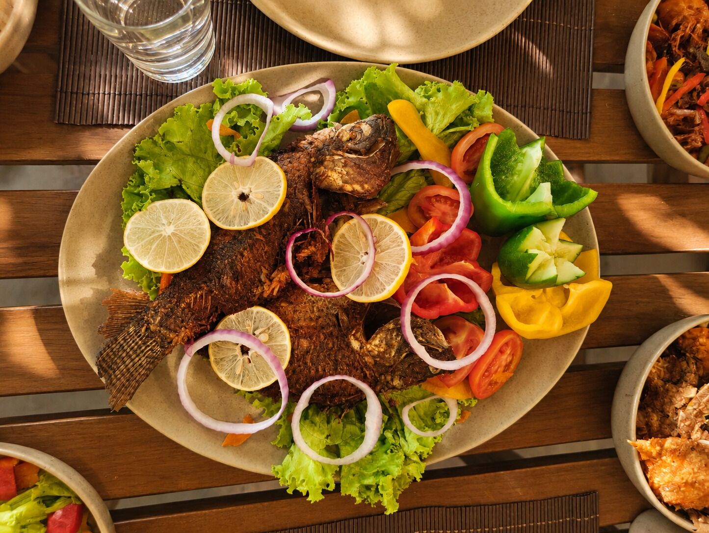 Un plato de comida con un pescado entero, verduras y rodajas de limón.