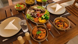 A wooden dining table with various dishes, including seafood and salads, and two plates with napkins. - J Villa Sigiriya - Private Pool Chalets (sigiriya)