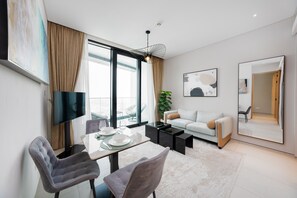 A modern living room with a dining area, large windows, a flat-screen TV, and a large mirror. - Chic Address JBR Haven w Marina View (Dubai)