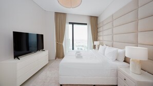 A hotel room with a flat-screen TV, a large bed with white bedding, a bedside table with a lamp, and a view of the city through a large window. - Chic Address JBR Haven w Marina View (Dubai)