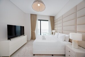 Ein Hotelzimmer mit Flachbildfernseher, einem großen Bett mit weißer Bettwäsche, einem Nachttisch mit Lampe und Blick auf die Stadt durch ein großes Fenster.