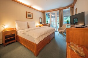 A hotel room with a wooden bed, a desk with a chair, a television, and a window with curtains.