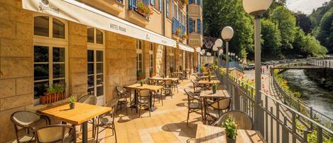 A hotel patio with outdoor seating, a river view, and a stone facade.