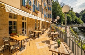 A hotel patio with outdoor seating, a river view, and a stone facade.