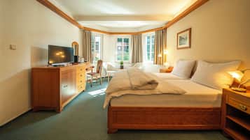 A hotel room with a bed, a desk with a television, a chair, a nightstand with a lamp, and a window with curtains.