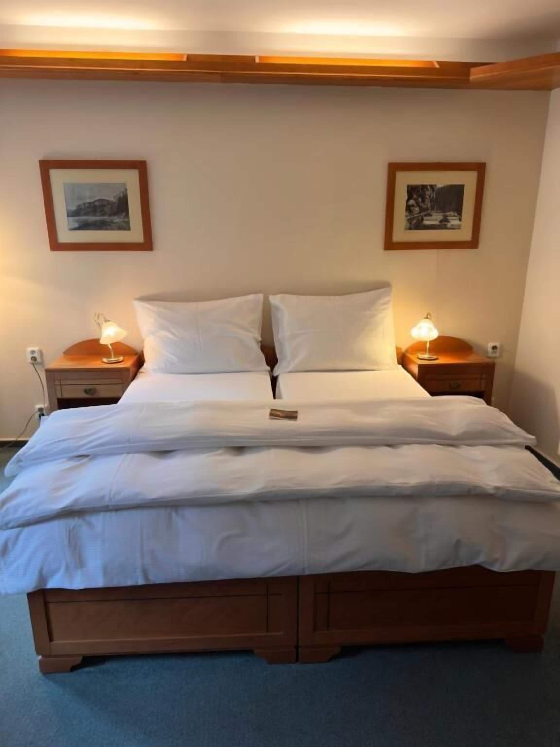 Een tweepersoonsbed met houten frame, twee nachtkastjes met lampen, en twee ingelijste foto's aan de muur.