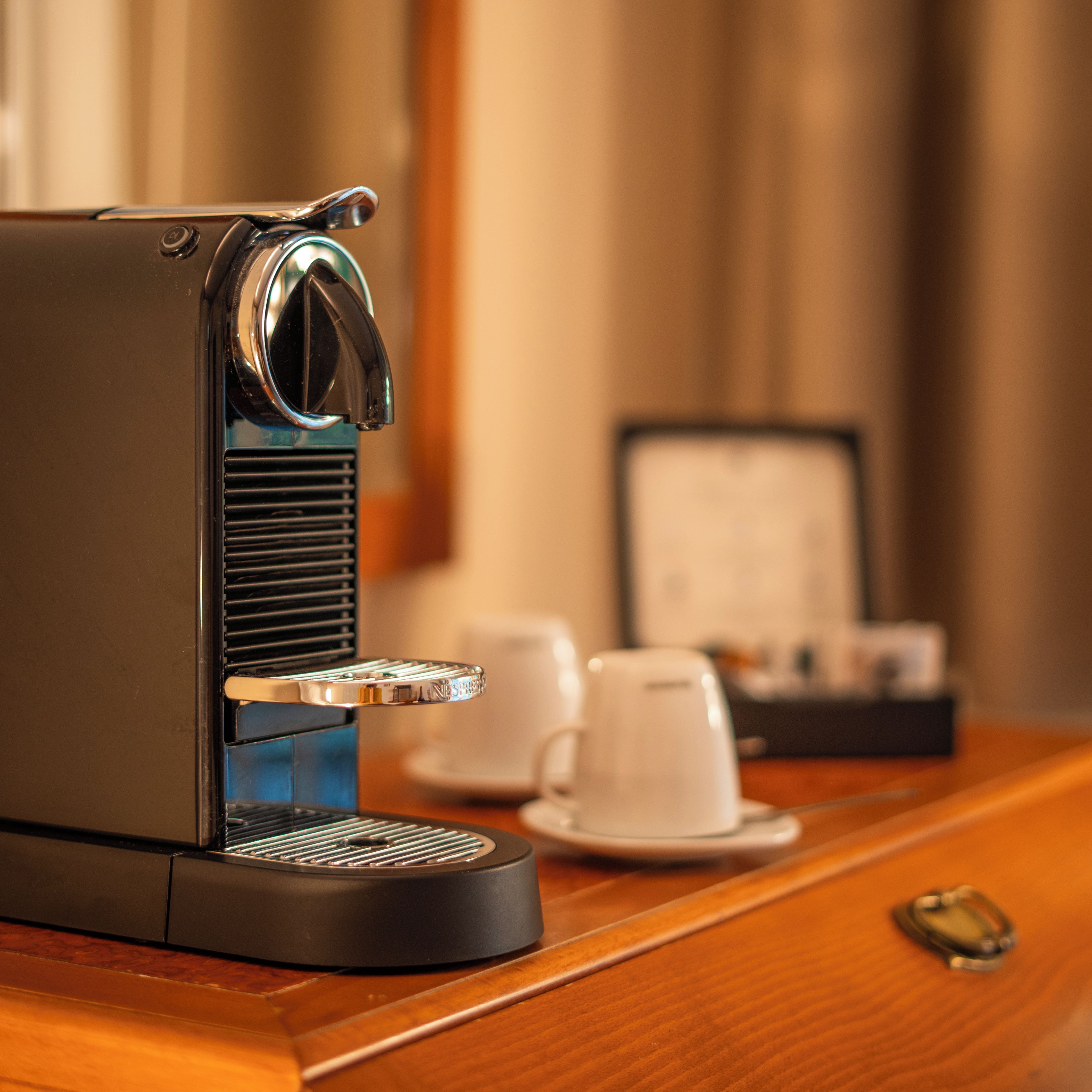 A coffee machine on a wooden table with a cup and saucer, a napkin holder, and a small object on the table.