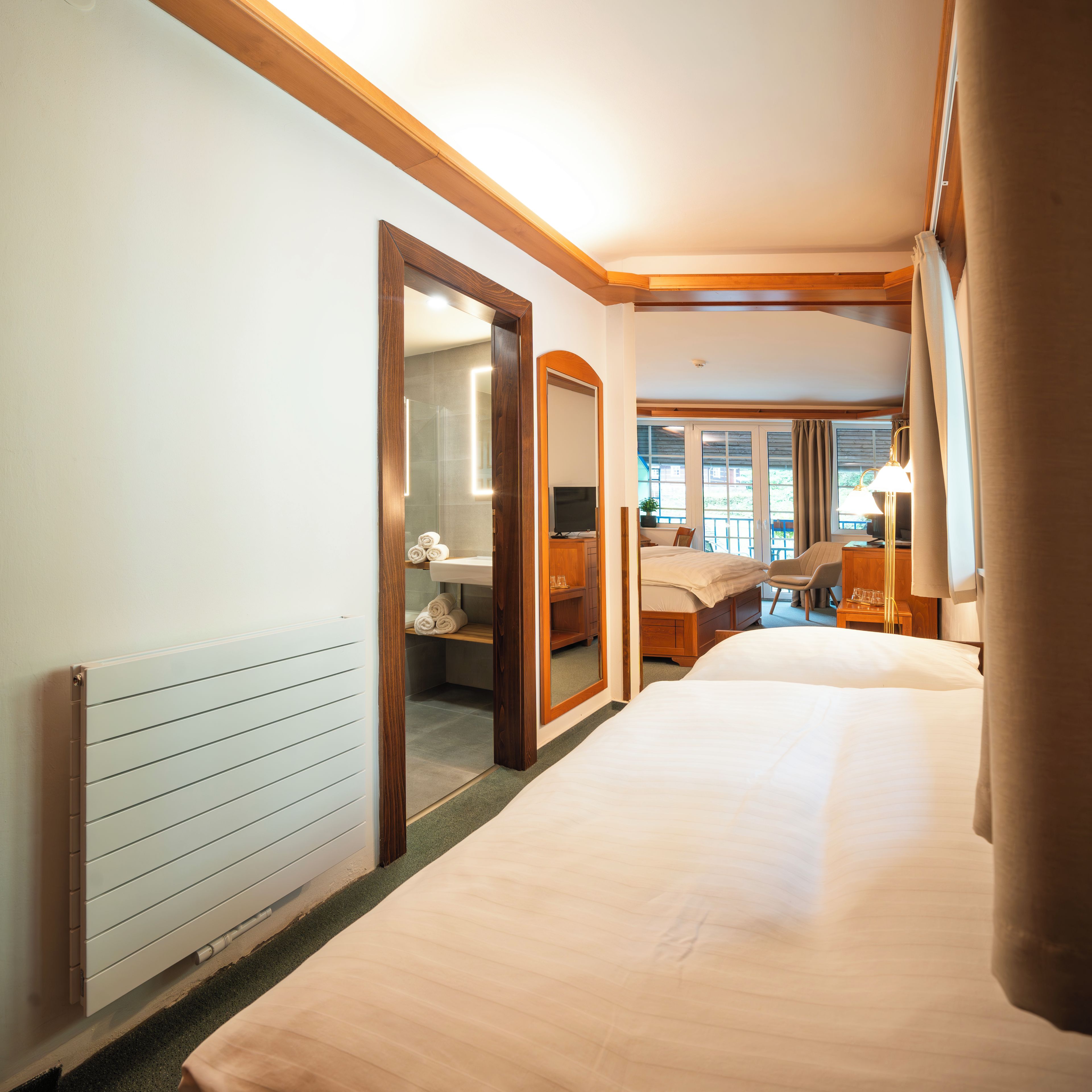 Een hotelkamer met een groot bed, een houten kledingkast, een spiegel en uitzicht op het omliggende landschap.