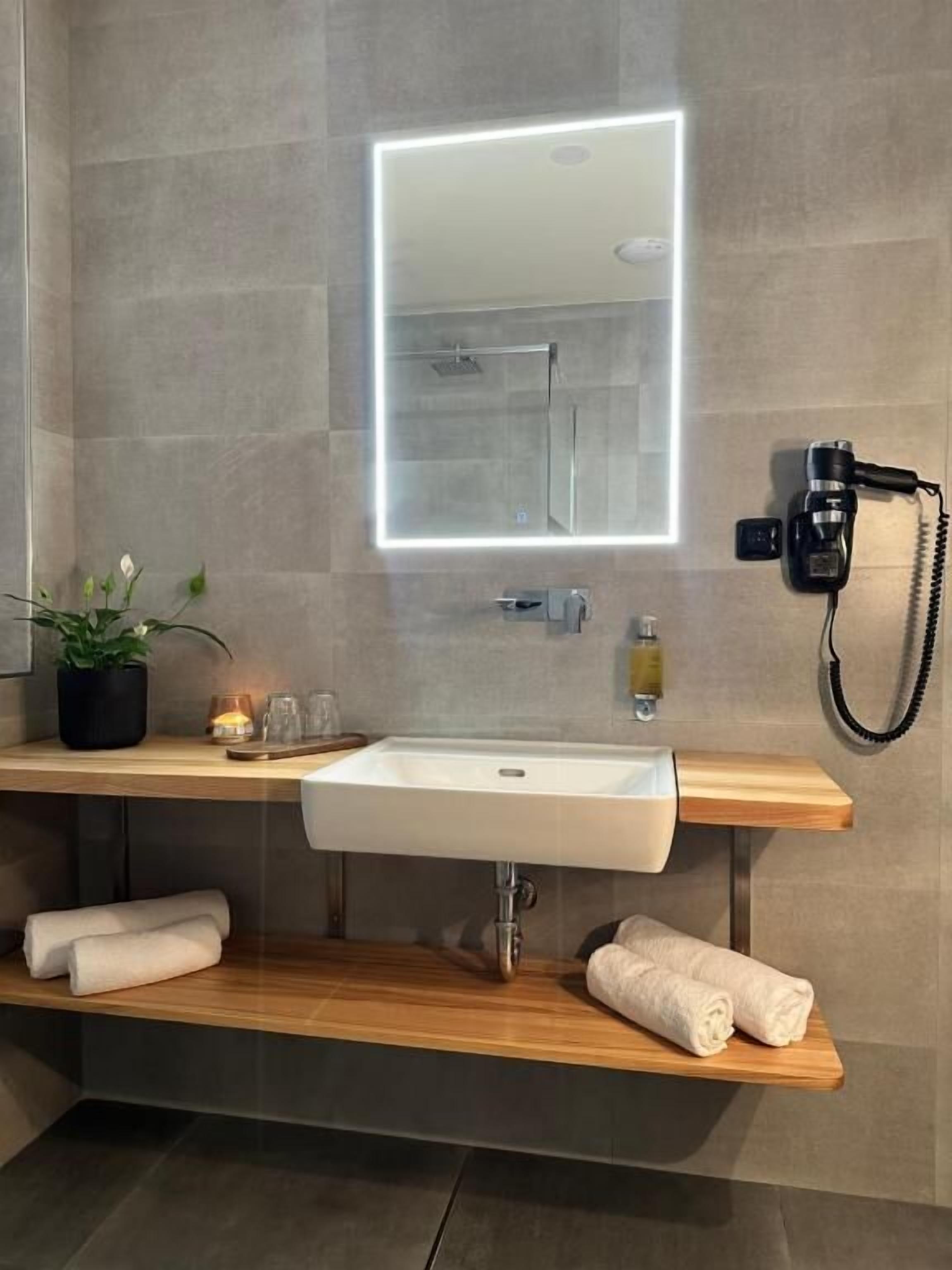 Une salle de bain moderne avec un grand miroir, un lavabo et un sèche-cheveux fixé au mur.